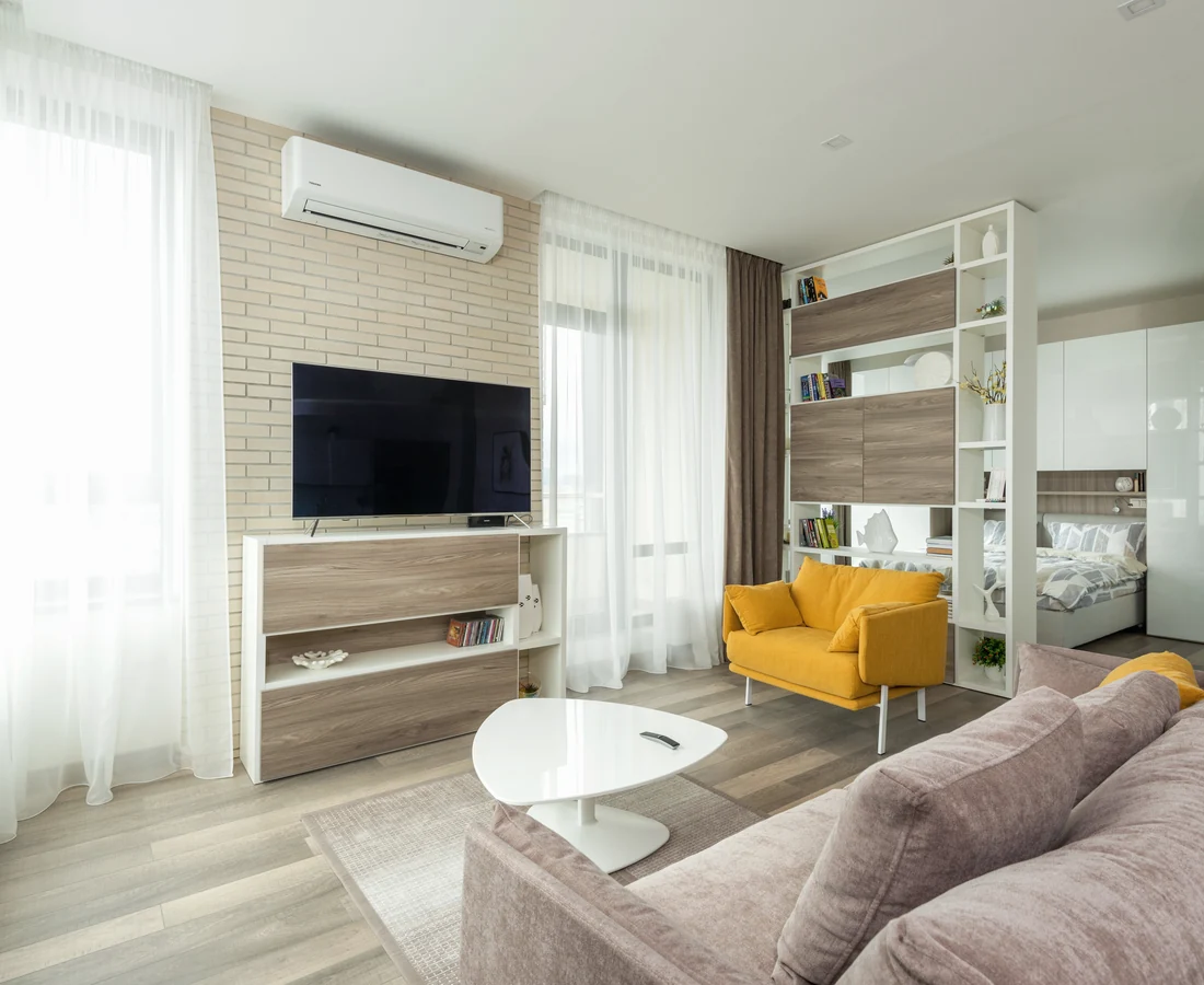 Heller kompakter Wohnraum mit Sofa, Sessel und offenem Schlafbereich